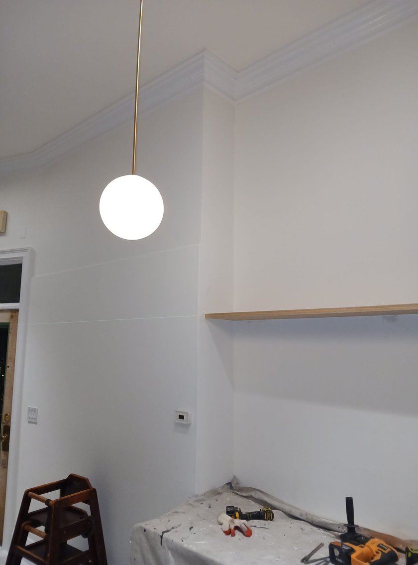 High-ceiling room with freshly painted white walls, new crown molding, hanging globe pendant light, and a long floating wood shelf