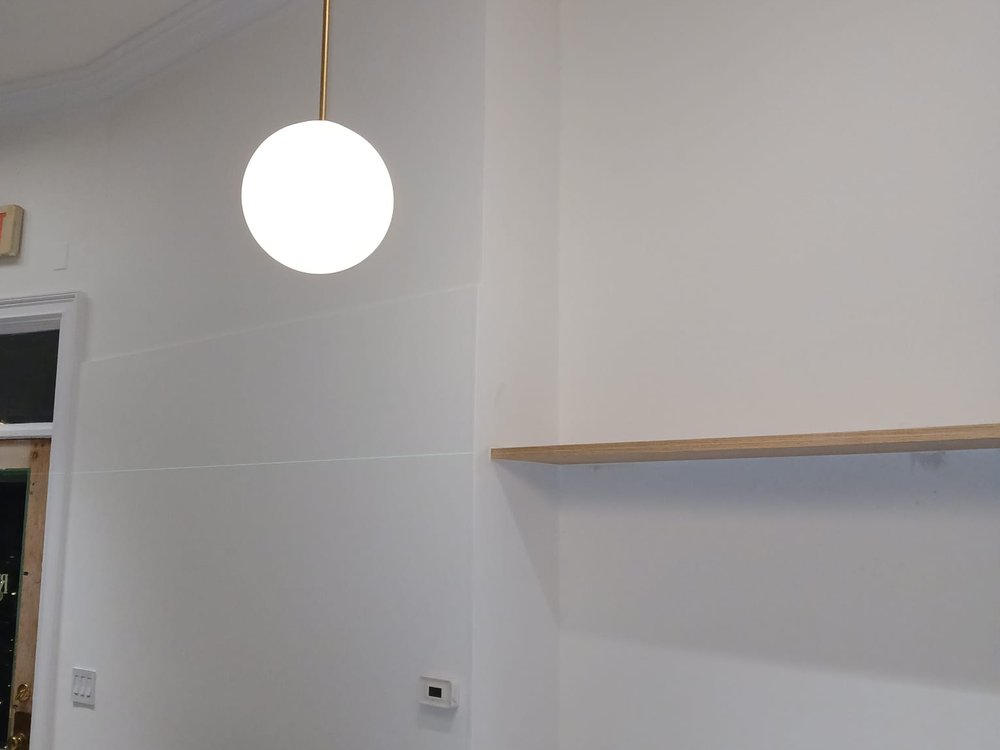 Freshly drywalled high-ceiling room with new crown molding and a custom floating wood shelf